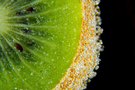 Kiwi sliced water bubbles dark black background texture close-up macro