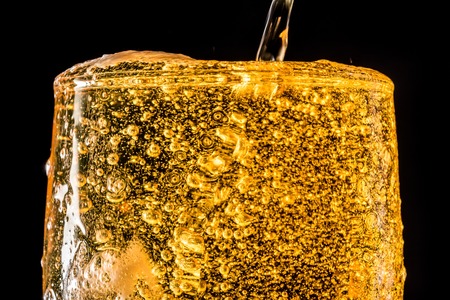 Stream of beer being pouring into a glass with beer and foam isolated on black background, closeup...