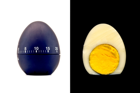 Timer as a black egg isolated on a white background and sliced boiled cooked egg refined with yolk on a black backgroundの写真素材