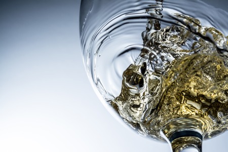 Stream of white wine pouring into a glass, white wine splash on grey backgroundの写真素材