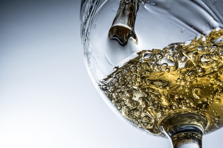 Stream of white wine pouring into a glass, white wine splash on grey backgroundの写真素材