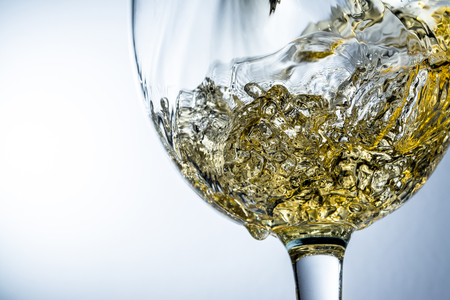 Stream of white wine pouring into a glass, white wine splash on grey backgroundの写真素材
