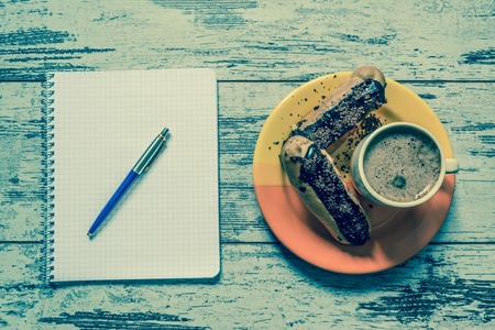 Coffee, cake, eclair with chocolate, notebook and pen close-up on vintage wooden background. Top view. Vintage style.の写真素材
