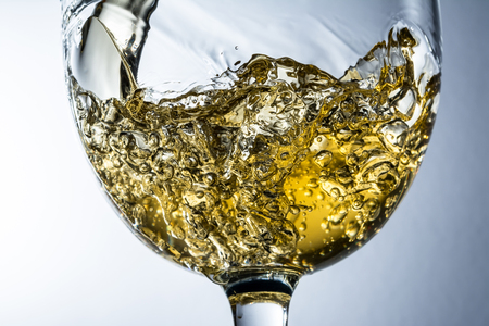 White wine splash on grey background, stream of white wine pouring into a glass.の写真素材
