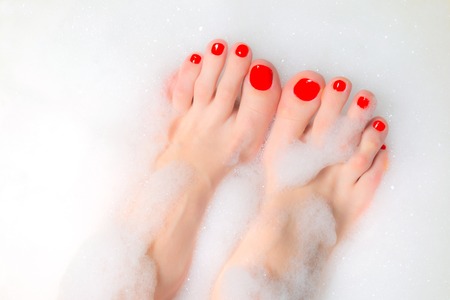 Feet of a young girl with red nails in a thick foamの写真素材