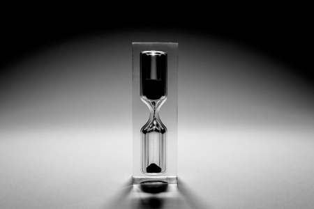 Hourglass sandglass with shadows. Old retro style vintage photo. Sand texture, falling sand.