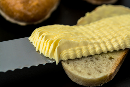 Butter with beautiful stains and a knife on a piece of bread close-up on a dark backgroundの写真素材