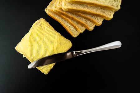 Butter with beautiful stains and a knife on a piece of bread close-up on a dark background