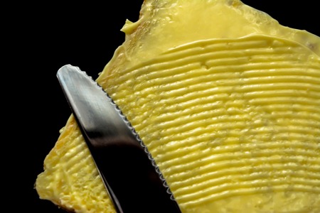 Butter with beautiful stains and a knife on a piece of bread close-up isolated on a black backgroundの写真素材