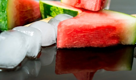 watermelon cut slice on a stick from ice cream in ice cube close-up with reflection on dark backgroundの写真素材