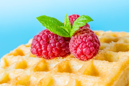 Sweet toast waffle breakfast with raspberries and sprig of mint leaves on top macro close-up on blue backgroundの写真素材