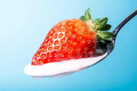 Strawberry on a spoon with strawberry pink yogurt cream close-up on blue backgroundの写真素材