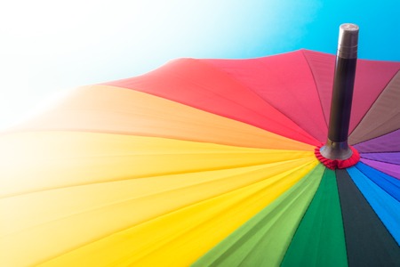 Multi-colored colorful umbrella with all colors of the rainbow in sunlight on a blue background. Bright texture background.の写真素材