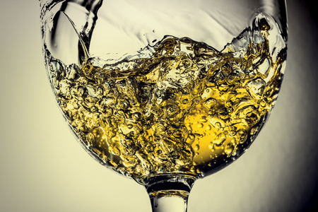 Stream of white wine pouring into a glass, white wine splash close-up on a grey background. Black and white photo with color of wine. Vintage, grunge, old, retro style.の写真素材
