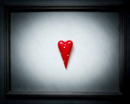 A red heart symbol on a white vintage background with paint stains in a vintage frame with dim lights around the edges.の写真素材