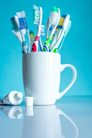 Multi-colored toothbrushes in a white mug close-up in the bathroom on a mirror table on a blue background.の写真素材