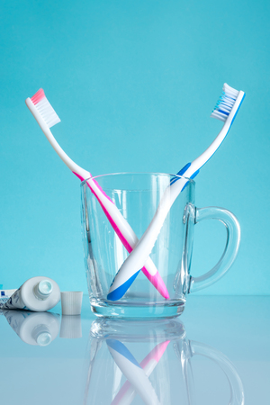 Multi-colored toothbrushes in a transparent stylish mug glass close-up in the bathroom on a blue background.の写真素材