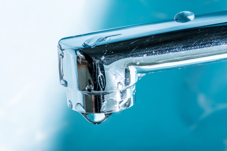 A drop of water hangs out of a modern chrome plated water tap faucet macro close up.の写真素材