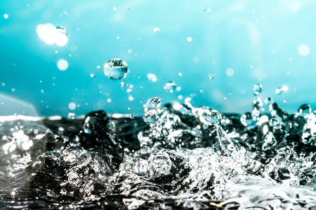 Drops of water close-up macro with a sunlight fall on the heavy splash water surface on a blue backgroundの写真素材