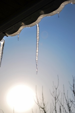 Icicles hanging from the roof in the rays of the sun against the blue clear sky