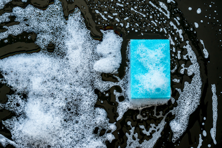 Blue sponge with beautiful divorces with foam close-up on a black glass background. Top view.の写真素材