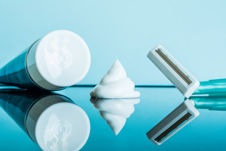 Regular disposable razor and shaving cream in a modern bathroom on a glass reflective surface against a blue background.の写真素材