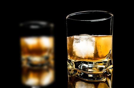 Whiskey with ice close up on a glass table isolated on a black backgroundの写真素材