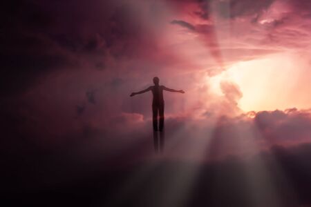 Silhouette of a man flying up in the sky in the bright rays of the sun with arms spread apart.
