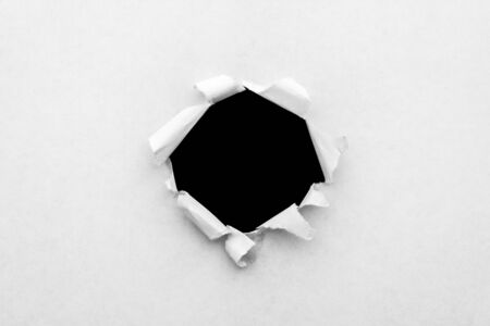 A round hole in white paper with torn edges and a black isolated background inside.