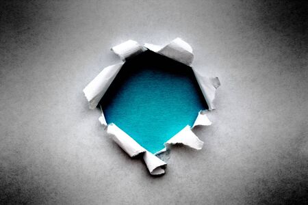 A hole in vintage paper with torn edges close-up with a blue azure color background inside.の写真素材