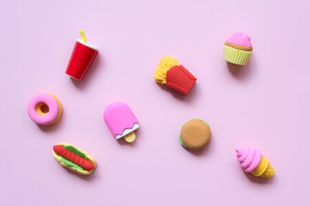 A variety of toy fast food and different sweets in miniature with shadows on a soft pink background
