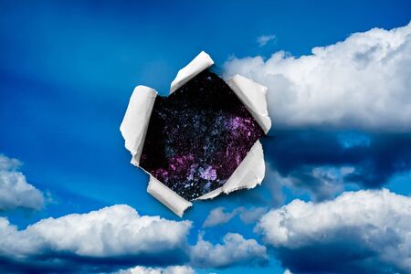 A hole in the day sky with torn edges, as if on paper, with a view into space with stars, nebulae and galaxies. The concept of global climate change on Earth, global warming, a hole in space and time.の写真素材