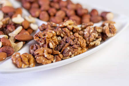 Various nuts close-up on a white plate on a white wooden table.