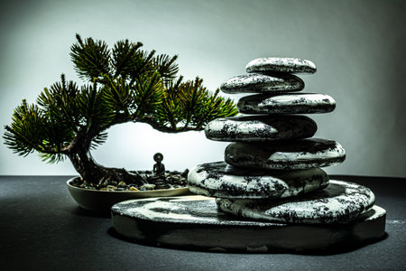 A meditative composition of flat stones stacked on top of each other next to a small bonsai tree, under which a man sits in the lotus position. Photo on the topic of yoga, meditation, relaxation.の写真素材