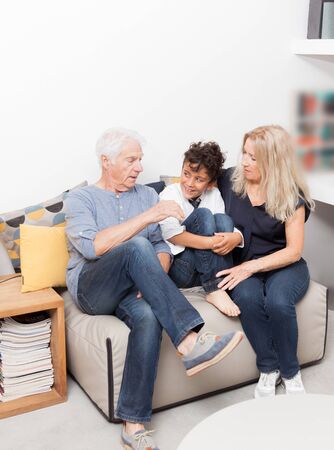 Boy with her grandmother and his grandfather on sofa. Seniors with grandchild in living room....
