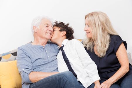 Boy kissing his grandfather. Seniors with grandchild on sofa. Family, sharing and joy concept.の写真素材