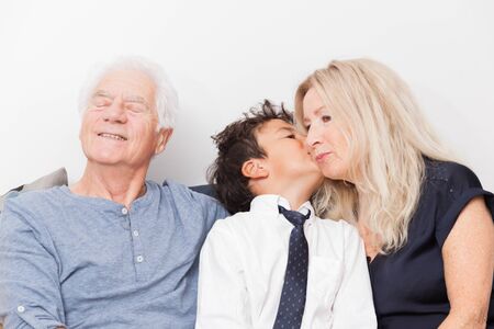 Boy kissing her grandmother. Seniors with grandchild on sofa. Family, sharing and joy concept.の写真素材