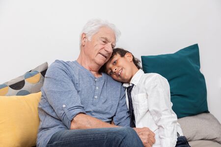 Happy boy cuddles his grandfather on a sofa. Concept of tenderness, family and joy.の写真素材