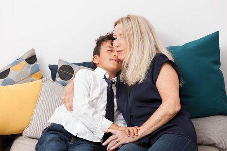 Happy boy cuddles her grandmother on a sofa. Concept of tenderness, family and joy.の写真素材