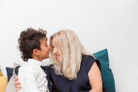 Happy boy kissing her grandmother on a sofa. Concept of tenderness, family and joy.の写真素材