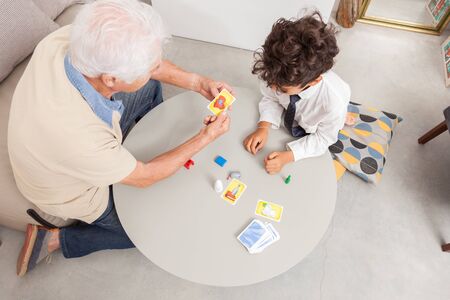 Boy playing board game with his grandfather.Cards and wooden objects.の写真素材