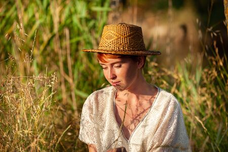 WELLNESS, RELAXATION, WOMAN WITH A STRAW HAT IN THE GRASS IN THE COUNTRYSIDEの写真素材