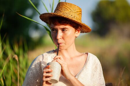 WOMAN WITH STRAW HAT DRINKING FROM STRAW IN THE COUNTRYSIDEの写真素材