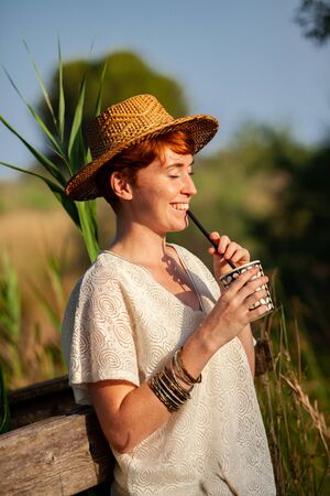 WOMAN WITH STRAW HAT DRINKING FROM STRAW IN THE COUNTRYSIDEの写真素材