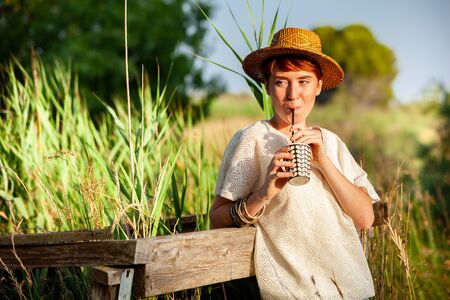 WOMAN WITH STRAW HAT DRINKING FROM STRAW IN THE COUNTRYSIDEの写真素材