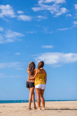 Complicity moment beetwen two girls best friends at the beach. Beautiful young women facing the sea.の写真素材