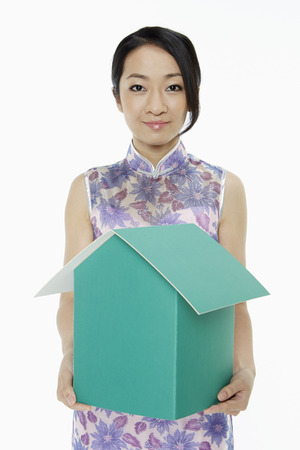 Woman in traditional clothing holding up a cardboard houseの写真素材