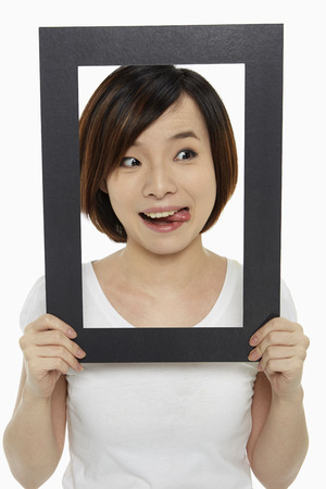Woman holding up a black picture frame, sticking her tongue outの写真素材