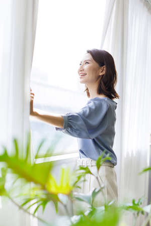 Young Asian woman looking out from the windowの写真素材