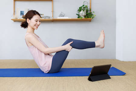 Young Asian woman practicing yoga while watching video on tablet computerの写真素材